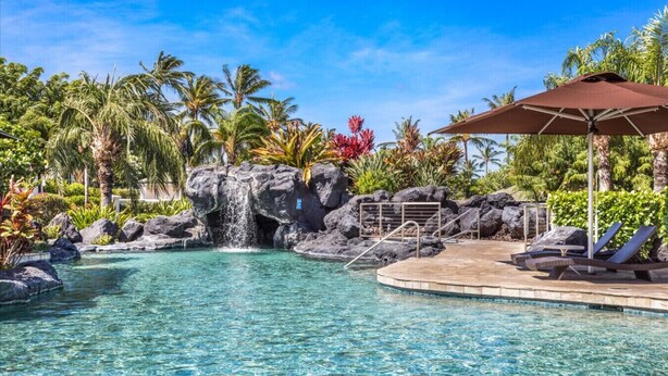 A clear pool with a waterfall feature, lounge chairs, and a shaded area with an umbrella. - The Islands M2 Oasis at Mauna Lani Resort (Kamuela)