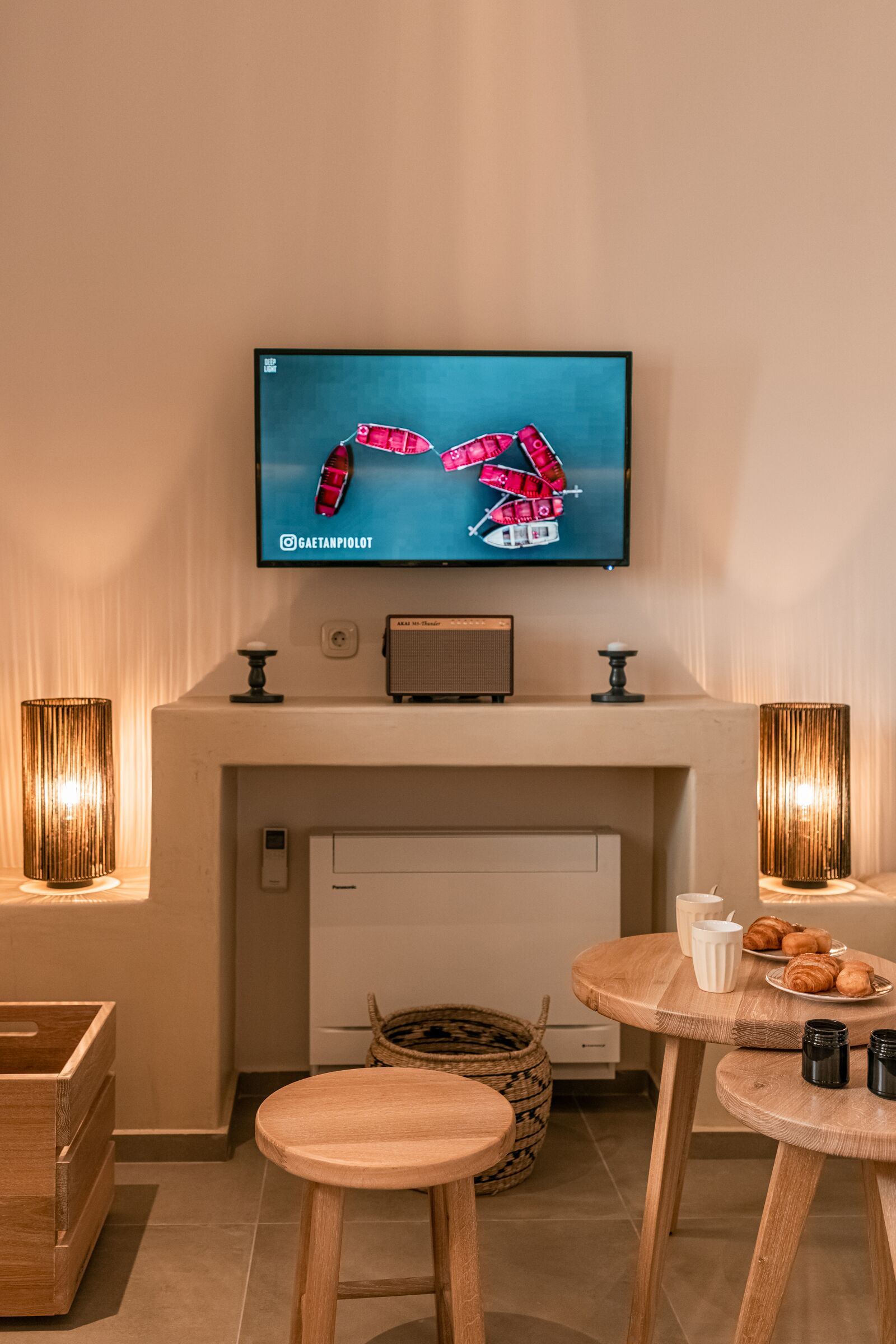 A modern living room with a flat-screen TV mounted above a fireplace, wooden furniture, and a basket on the floor.