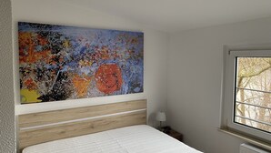 Un dormitorio con cama, una mesita de noche, una lámpara y un cuadro abstracto de gran tamaño en la pared.