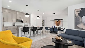 A modern living room with a yellow armchair, a blue sofa, and a coffee table with a decorative vase. - Betty's Bliss | Peaceful retreat w pool & high-end decor - near shopping & parks (Orlando)