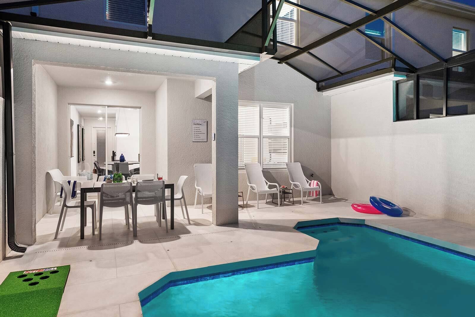 A modern indoor pool area with a dining table and chairs, lounge chairs, and a pool with a clear blue edge.
