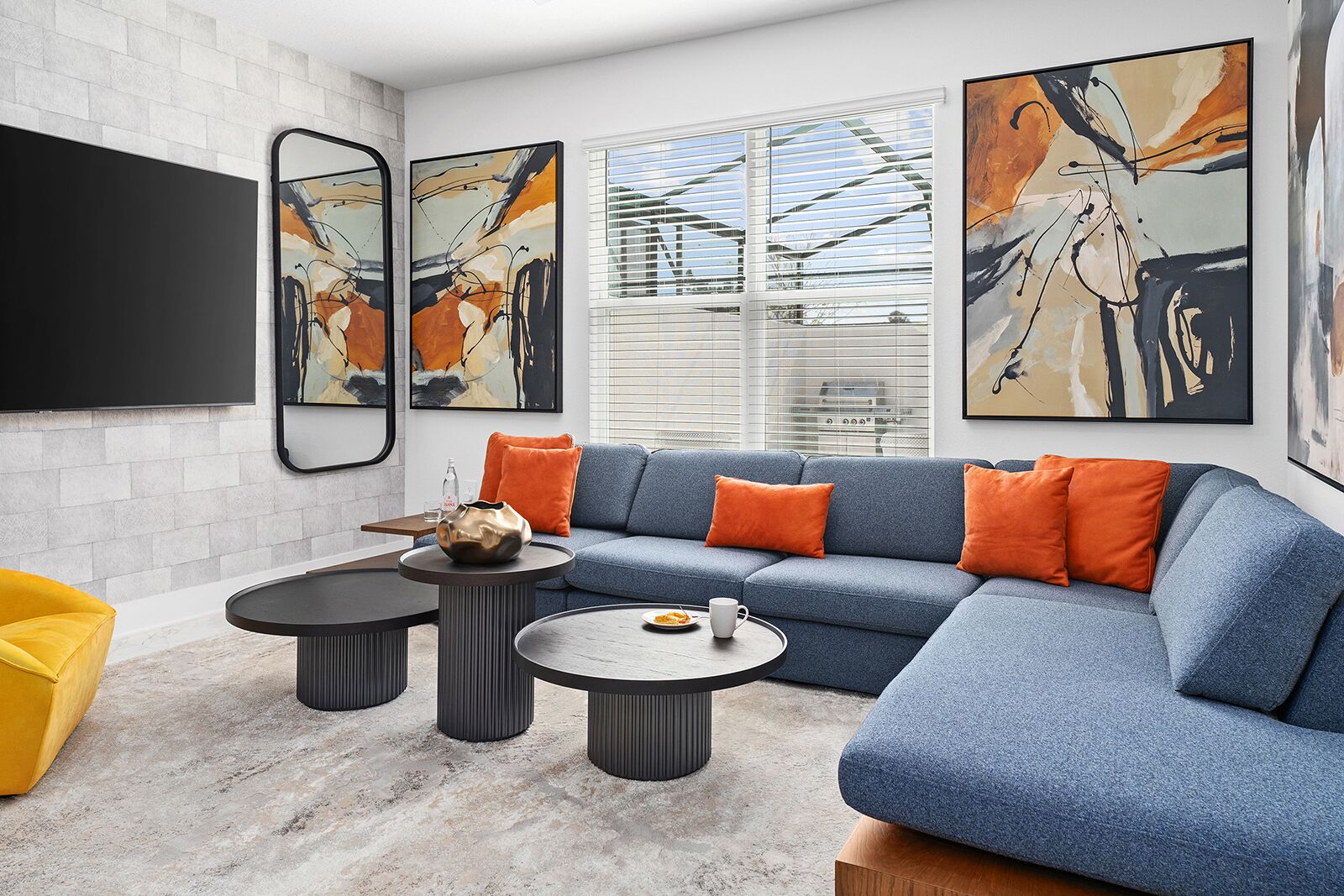 Un salon moderne avec un canapé d’angle, deux petites tables rondes et un fauteuil jaune.