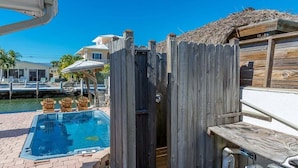 A wooden fence enclosing a swimming pool area with a hot tub and lounge chairs.