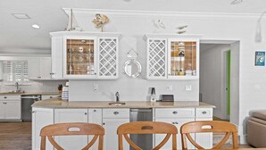 A modern kitchen with white cabinetry, a central island with chairs, and a view into the adjacent dining area.