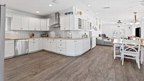 A modern kitchen with white cabinetry, a built-in oven, and a dining area with a wooden table and chairs.