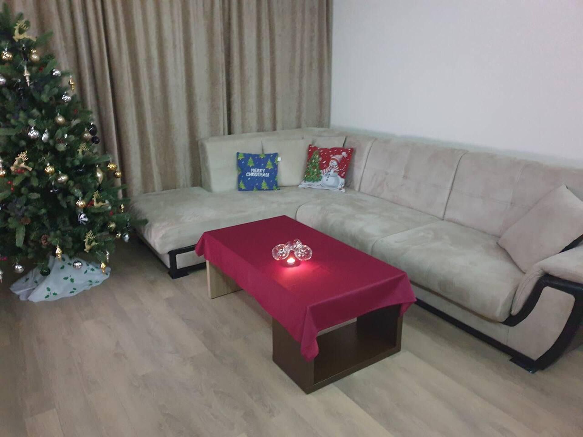Ein Wohnzimmer mit einem beigen Sofa, einem roten Tisch und einem Weihnachtsbaum.