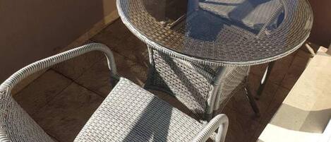 Un balcón con mobiliario de mimbre, que incluye una mesa redonda y dos sillas.