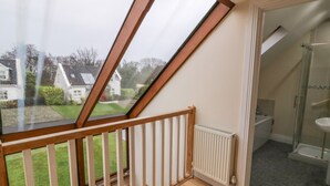Een kamer met een schuine kap, een houten vloer, een radiator en een douchecabine van glas.