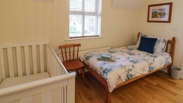 A bedroom with a wooden bed, a crib, a window with blinds, and a framed picture on the wall.