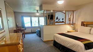 A bedroom with a large bed, a wooden dresser, a desk, and a chair. There is a window with a view of trees. - Manhattan Beach Lodge (Crosslake)