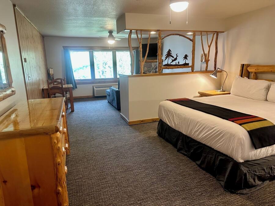 Une chambre avec un grand lit, une commode en bois, un bureau et une chaise. Il y a une fenêtre donnant sur les arbres.