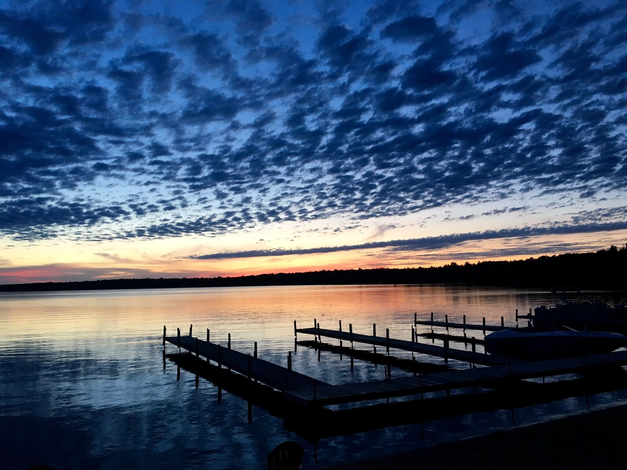 Um lago tranquilo ao entardecer, com um cais de madeira que se projeta sobre a água.