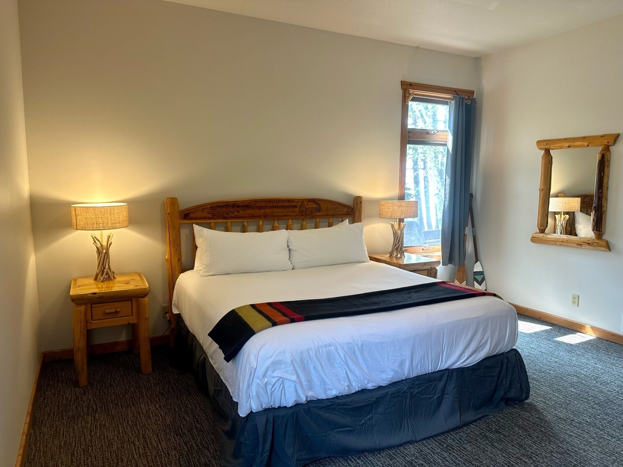 A bedroom with a large bed, two bedside tables, a window with curtains, and a mirror on the wall.