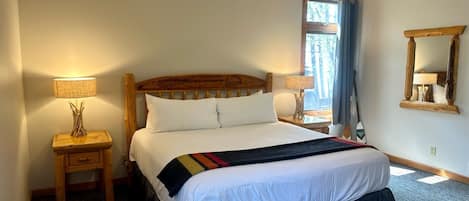 A bedroom with a large bed, two bedside tables, a window with curtains, and a mirror on the wall.