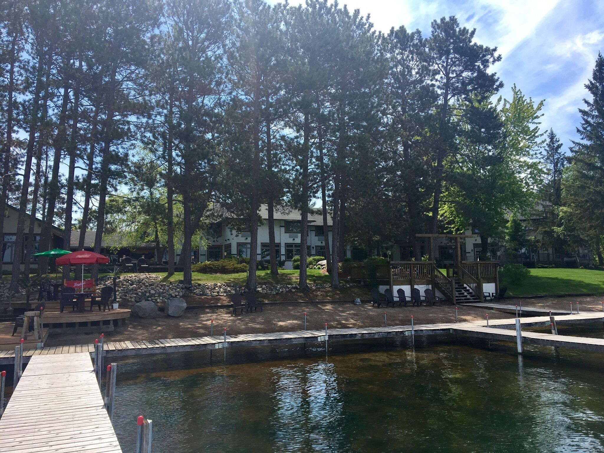 Un resort sul lago con un molo, area salotto esterna e una piscina circondata da alberi alti.