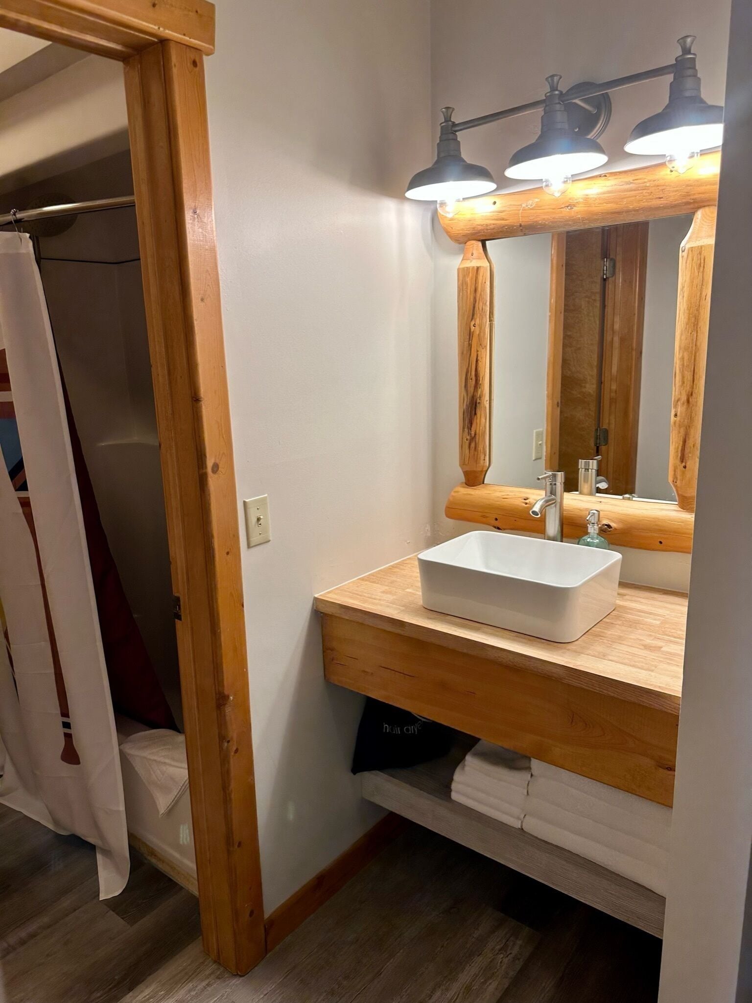 A bathroom with a wooden vanity, a white sink, and a mirror with three lights.