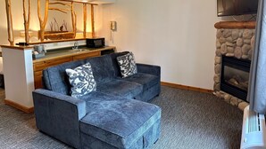 A cozy living room with a stone fireplace, a flat-screen TV mounted above it, a wooden coffee table, and a blue sofa with patterned cushions. - Manhattan Beach Lodge (Crosslake)