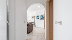 Un couloir avec une porte, un porte-manteau, un lit et des œuvres d’art abstrait accrochées au mur.