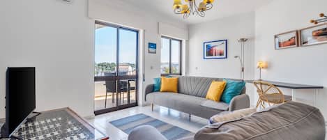 A modern living room with a sofa, a television, a chess table, and a balcony with a view.