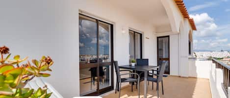 A balcony with a table and chairs, a potted plant, and a view of a cityscape.