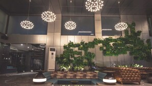 Un hall con candelabros modernos, una zona de estar y una pared con plantas verdes.