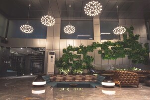 Um hall com lustres modernos, área de estar e parede com plantas verdes.