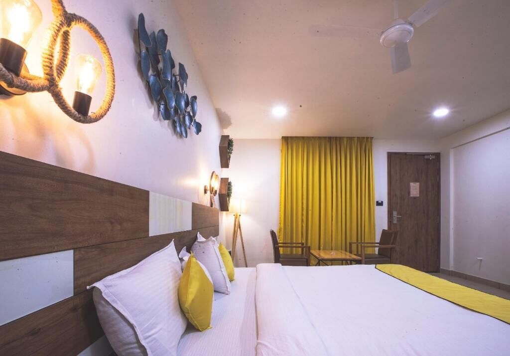 Camera d'albergo con testiera in legno, letto con biancheria da letto bianco e giallo, una scrivania con sedia, una tenda gialla e un lampadario fissato alla parete.