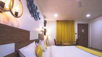 Camera d'albergo con testiera in legno, letto con biancheria da letto bianco e giallo, una scrivania con sedia, una tenda gialla e un lampadario fissato alla parete.