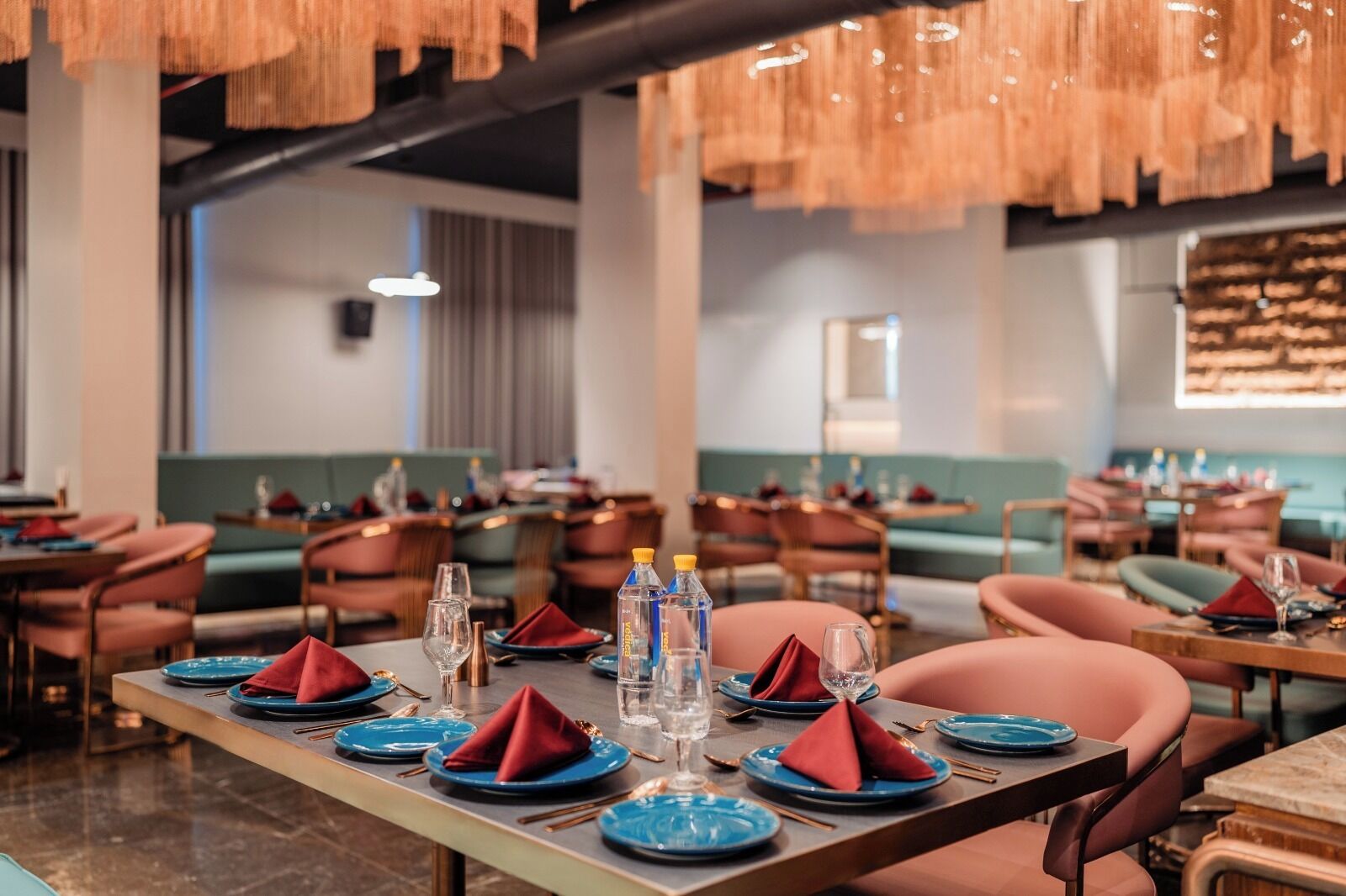 Un restaurante con mesas dispuestas, con platos azules, servilletas rojas y botellas de agua.