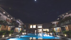 Vista nocturna de un hotel con piscina, varios pisos y balcones bien iluminados.