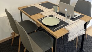 Ein Essbereich mit einem Holztisch, vier grauen Stühlen, einem Laptop, einem Glas und einem Teller.