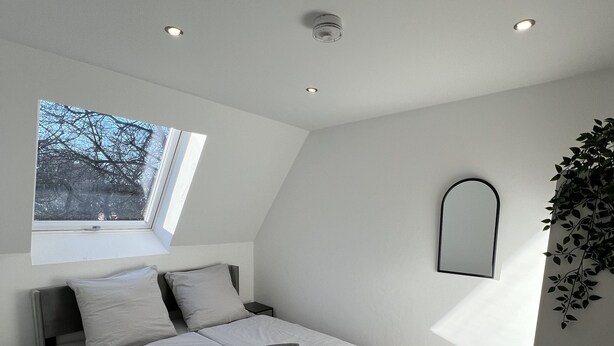 Ein modernes Schlafzimmer mit Schlafkoje, Dachfenster, Nachttisch und Spiegel an der Wand.