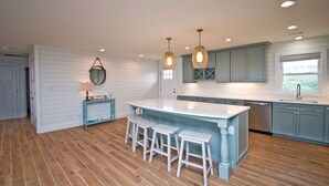 Cocina con una isla grande, taburetes de bar, luces colgantes y vistas al exterior a través de una ventana.