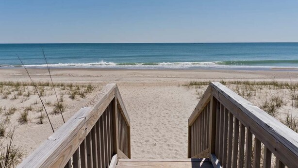 Un muelle de madera que conduce a una playa de arena con vistas al océano.