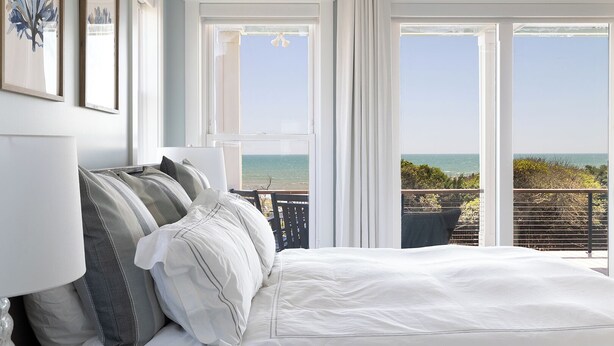 Ein Schlafzimmer mit einem großen Bett, Meerblick und einem Balkon mit Geländer.