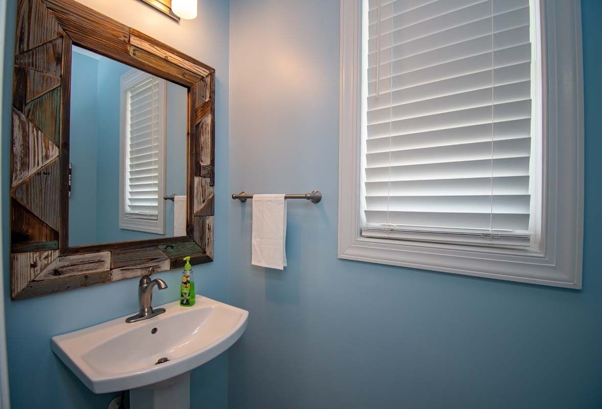 A bathroom with a white sink, a wooden-framed mirror, and white window blinds.