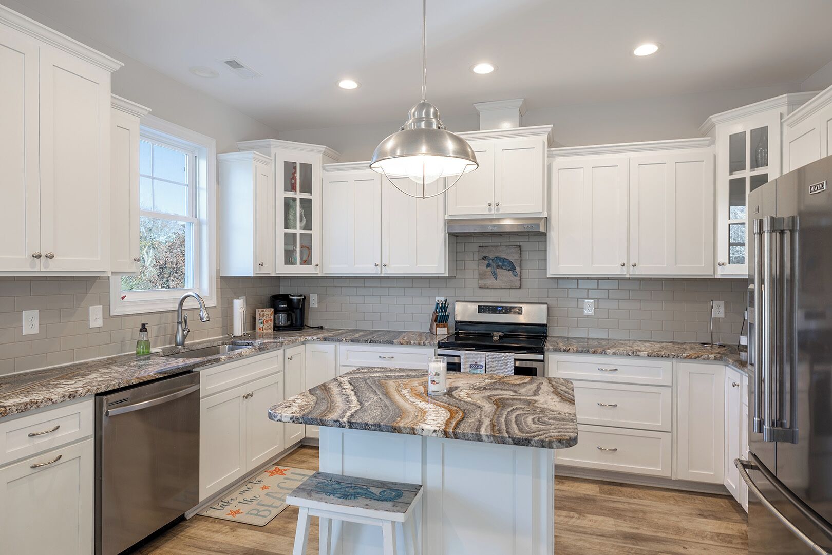 A modern kitchen with white cabinetry, a granite countertop, stainless steel appliances, and a central island.