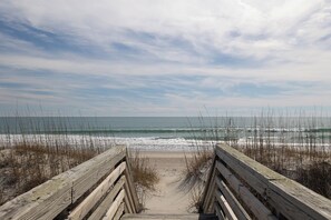 A wooden boardwalk leading to a beach with waves and a cloudy sky.