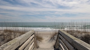 A wooden boardwalk leading to a beach with waves crashing onto the shore and a clear sky above. - Sassy Seagull West, Oceanfront Duplex in Emerald Isle, NC! (Emerald Isle)