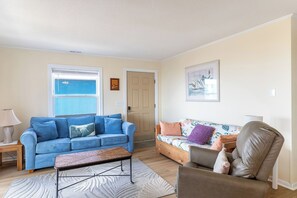 A living room with a blue sofa, a floral sofa, a brown leather chair, a coffee table, and a door leading to another room.