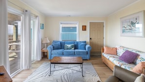 A living room with a blue sofa, a wooden coffee table, a patterned rug, and a floral sofa. - Sassy Seagull West, Oceanfront Duplex in Emerald Isle, NC! (Emerald Isle)