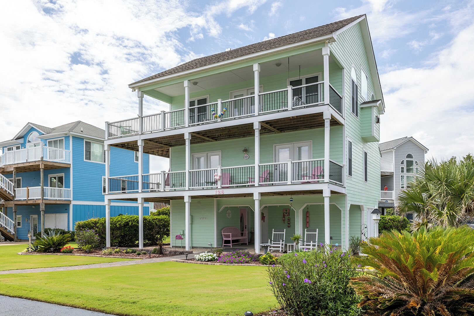 A multi-story building with a balcony on each floor, surrounded by well-maintained lawns and tropical plants.
