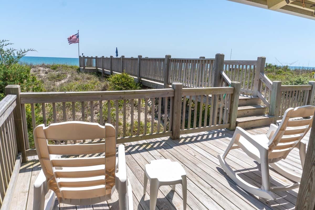 A wooden deck with a railing, a small table, and two rocking chairs.