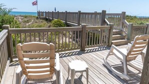 A wooden deck with a railing, a small table, and two rocking chairs. - Sea Castle East, Oceanfront Duplex in Emerald Isle, NC! (Emerald Isle)