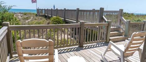 A wooden deck with a railing, a small table, and two rocking chairs.