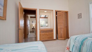 A bedroom with two beds, wooden furniture, and a hallway leading to another room. - Sea Castle West, Oceanfront Duplex in Emerald Isle, NC! (Emerald Isle)