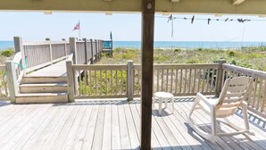 A wooden deck with a railing, a rocking chair, and a small table. - Sea Castle West, Oceanfront Duplex in Emerald Isle, NC! (Emerald Isle)