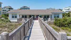A wooden boardwalk leading to a two-story building with a flat roof and multiple windows. - Sea Castle West, Oceanfront Duplex in Emerald Isle, NC! (Emerald Isle)