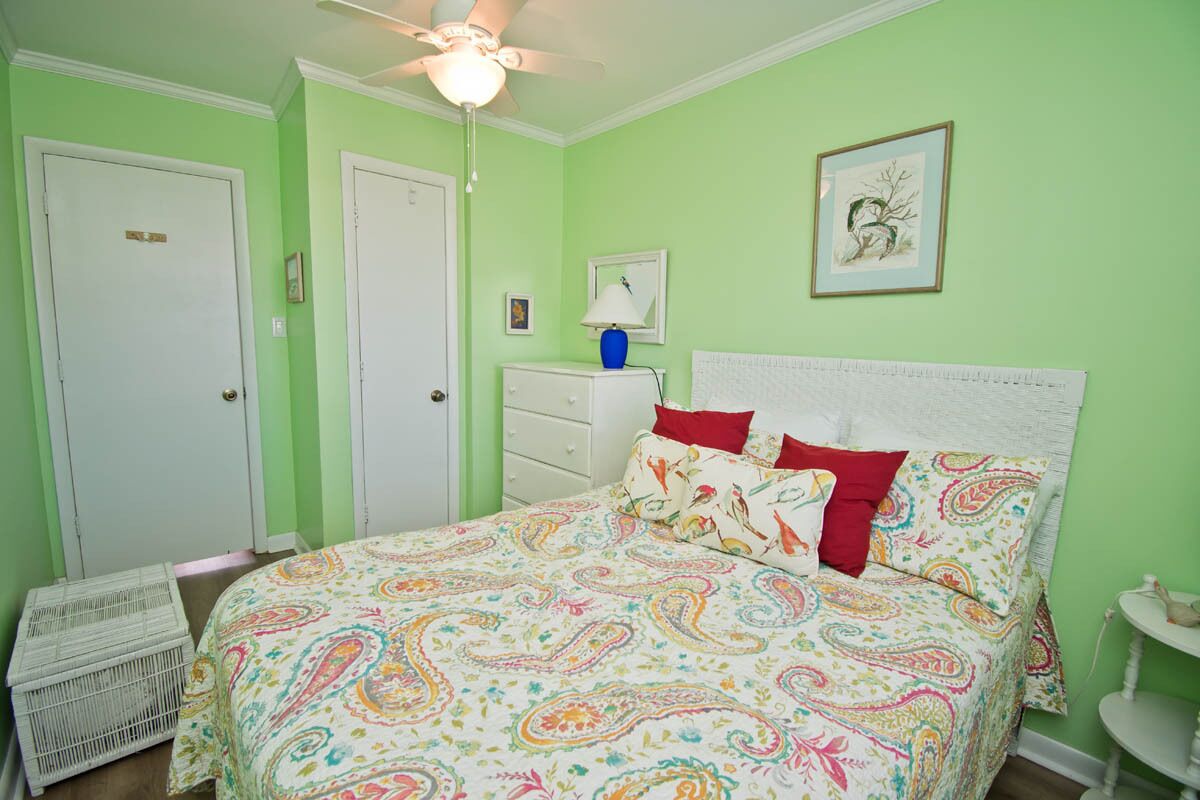 A bedroom with a bed, a ceiling fan, a dresser, and a framed picture on the wall.