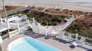 A pool area with lounge chairs and a deck overlooking a beach.